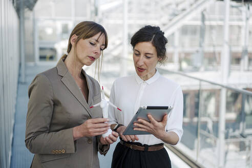 Two businesswomen with tablet and wind turbine model having a meeting at a greenhouse - JOSEF00710
