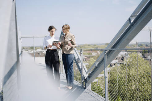Two businesswomen with tablet having a meeting on roof terrace - JOSEF00714