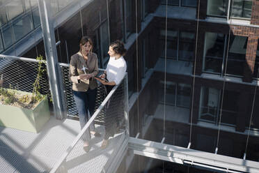 Zwei Geschäftsfrauen mit Tablet und Windradmodell bei einem Treffen auf dem Balkon eines Bürogebäudes - JOSEF00715