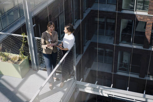 Two businesswomen with tablet and wind turbine model having a meeting on balcony of an office building - JOSEF00715