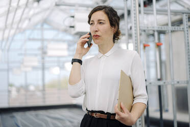 Serious businesswoman with clipboard on the phone - JOSEF00727