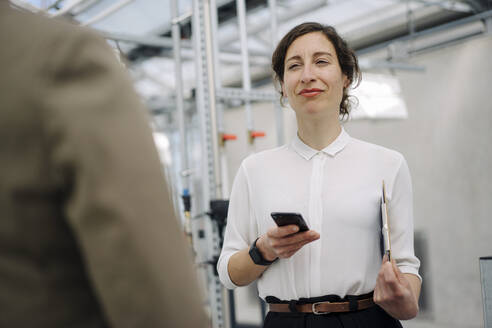 Portrait of businesswoman with cell phone looking at colleague - JOSEF00729