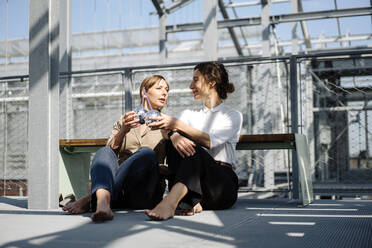 Zwei Geschäftsfrauen bei einem Drink an einer Metallkonstruktion im Freien - JOSEF00738