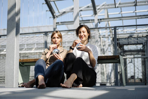 Two businesswomen having a drink at a metal construction outdoors - JOSEF00739