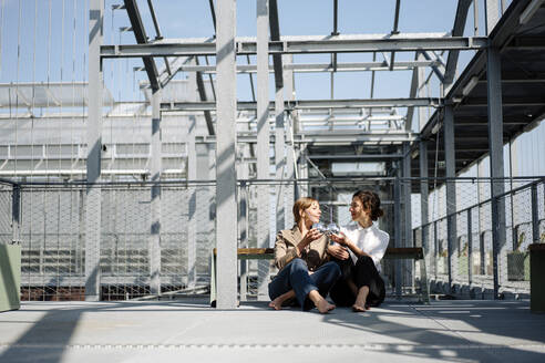 Two businesswomen having a drink at a metal construction outdoors - JOSEF00740