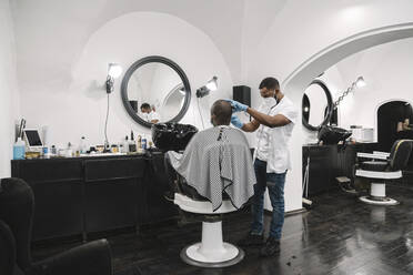 Friseur mit chirurgischer Maske und Handschuhen beim Haarschneiden eines Kunden - AHSF02537