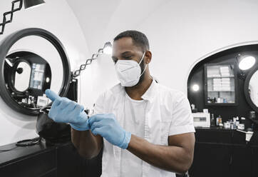 Friseur mit chirurgischer Maske zieht wiederverwendbare Handschuhe an - AHSF02550