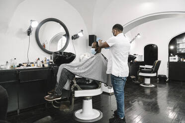 Litauen, Vilnius, Friseur mit chirurgischer Maske und Handschuhen beim Haarschneiden eines Kunden - AHSF02556