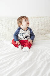 Porträt eines kleinen Jungen, der auf dem Bett sitzt und nach oben schaut - FLMF00218