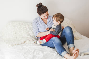 Glückliche Mutter sitzt auf dem Bett und spielt mit ihrem kleinen Sohn - FLMF00221