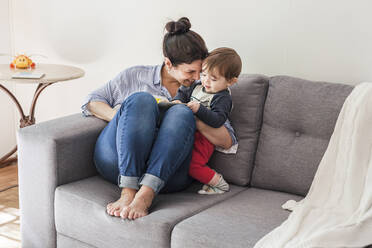 Happy mother sitting on couch cuddling her little son - FLMF00225