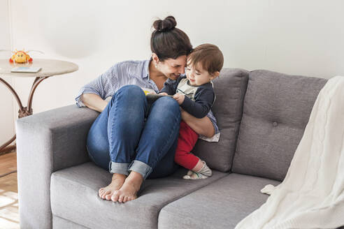 Glückliche Mutter sitzt auf der Couch und kuschelt mit ihrem kleinen Sohn - FLMF00225