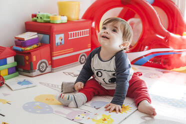 Portrait of baby boy sitting on the floor at home looking up - FLMF00227