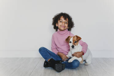 Porträt eines lächelnden kleinen Mädchens, das mit seinem Hund auf dem Boden sitzt - EBBF00076