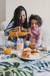 Mother and her little daughter sitting together on couch drinking juice and smoothies - EBBF00079