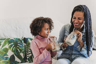 Laughing mother and her little daughter drinking smoothies at home - EBBF00082