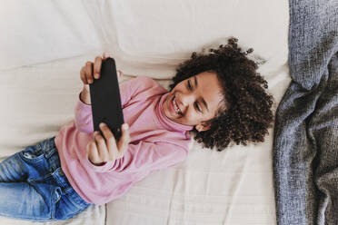 Portrait of happy little girl lying on the couch using smartphone - EBBF00090