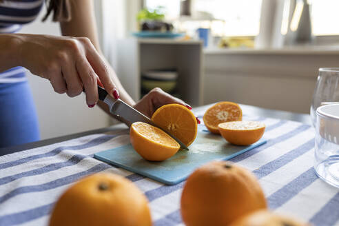 Frau schneidet frische Orangen für frisch gepressten Orangensaft - WPEF02894