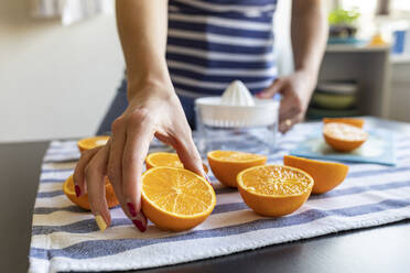 Frau bereitet frischen Orangensaft zu und nimmt eine in Scheiben geschnittene Orange - WPEF02896