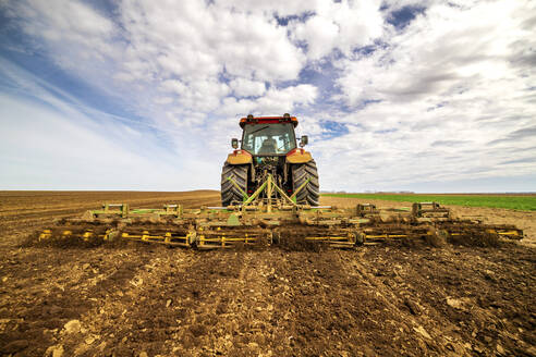 Rückansicht eines Landwirts im Traktor beim Pflügen eines Feldes im Frühling - NOF00092