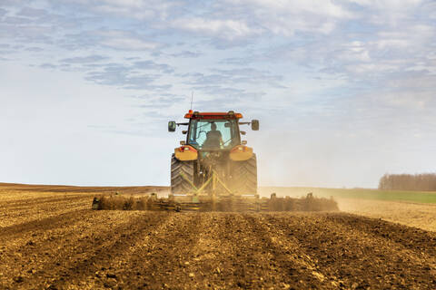 Rückansicht eines Landwirts im Traktor beim Pflügen eines Feldes im Frühling, lizenzfreies Stockfoto