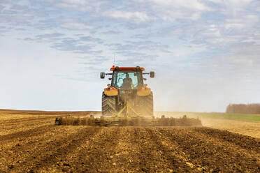 Rückansicht eines Landwirts im Traktor beim Pflügen eines Feldes im Frühling - NOF00094