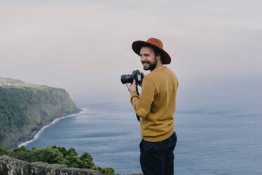 Lächelnder Mann mit einer Kamera an der Küste der Insel Sao Miguel, Azoren, Portugal - AFVF06299