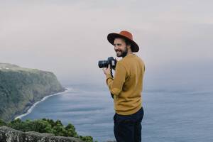 Smiling man with a camera at the coast on Sao Miguel Island, Azores, Portugal - AFVF06299
