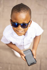 Porträt eines lächelnden kleinen Jungen mit Sonnenbrille und Smartphone - OCMF01223