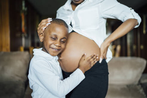 Kleiner Junge lauscht am Bauch einer schwangeren jungen Frau - OCMF01236