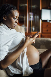 Pregnant young woman using cell phone on couch - OCMF01238