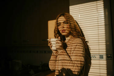 Portrait of beautiful blond woman drinking coffee in the kitchen in sunlight - GMLF00201