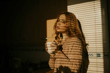 Portrait of beautiful blond woman drinking coffee in the kitchen in sunlight - GMLF00202