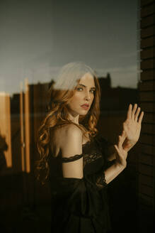 Porträt einer schönen blonden Frau in schwarzen Dessous hinter einer Fensterscheibe - GMLF00207