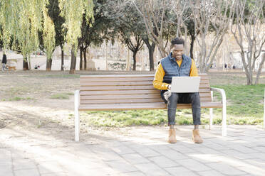 Young man sitting on park bench using laptop - JCZF00091