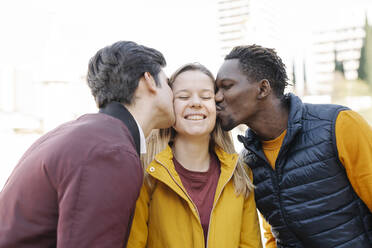 Two young men kissing smiling young woman outdoors - JCZF00100