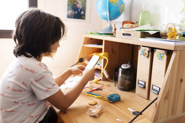 Boy sitting at desk at home using smartphone - VABF02970