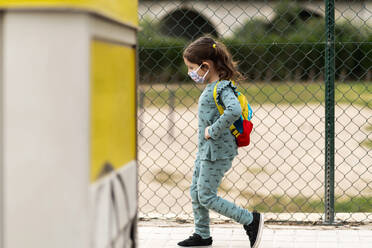 Girl wearing mask and walking with backpack outdoors - EGAF00111
