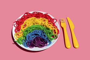 Teller mit regenbogenfarbenen Spaghetti vor rosa Hintergrund - GEMF03732