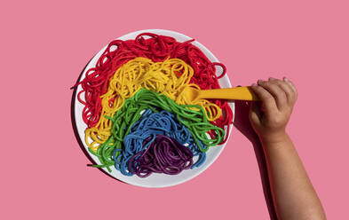 Hand eines kleinen Mädchens, das regenbogenfarbene Spaghetti isst - GEMF03734