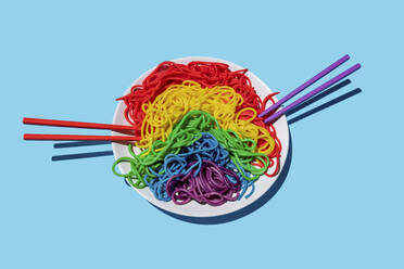 Teller mit regenbogenfarbenen Spaghetti vor blauem Hintergrund - GEMF03735