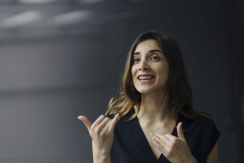 Porträt einer gestikulierenden jungen Geschäftsfrau vor grauem Hintergrund, lizenzfreies Stockfoto