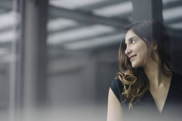 Portrait of smiling young businesswoman behind windowpane looking at distance - JOSEF00764