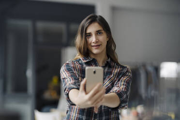 Portrait of smiling young woman taking selfie in a loft - JOSEF00794