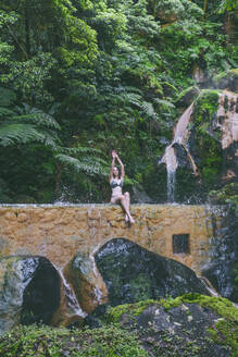 Junge Frau sitzt an einer heißen Quelle, Caldeira Velha, Insel Sao Miguel, Azoren, Portugal - FVSF00283