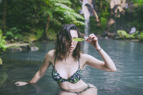 Junge Frau mit Blatt, die in einer heißen Quelle badet, Caldeira Velha, Insel Sao Miguel, Azoren, Portugal - FVSF00285