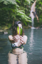 Junge Frau mit Blättern in der Hand beim Baden in einer heißen Quelle, Caldeira Velha, Insel Sao Miguel, Azoren, Portugal - FVSF00286