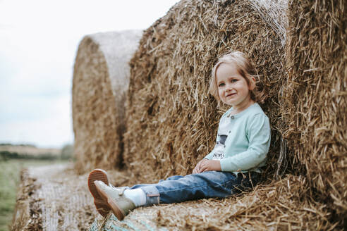 Porträt eines lächelnden Mädchens, das auf Strohballen sitzt - VBF00068