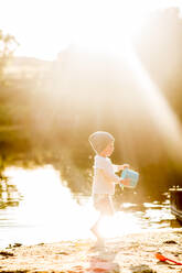 Sommer goldene Sonne Kleinkind spielt mit Eimer am See - CAVF81557