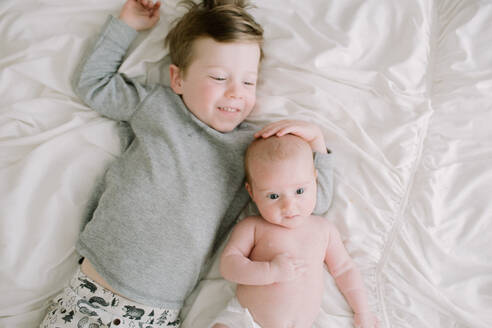 Großer Bruder und kleine Schwester auf dem Bett liegend von oben - CAVF81564